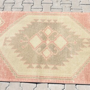 Puede incluir: Una alfombra vintage con un patr&oacute;n geom&eacute;trico en tonos rosa, beige y gris. La alfombra tiene un aspecto desgastado y es perfecta para a&ntilde;adir un toque de estilo bohemio a cualquier habitaci&oacute;n.