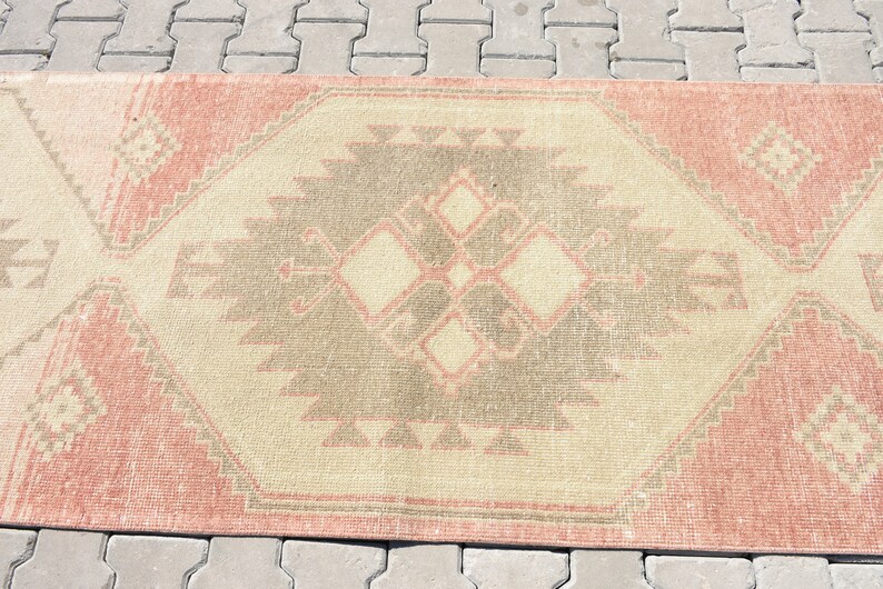 Puede incluir: Una alfombra vintage con un patr&oacute;n geom&eacute;trico en tonos rosa, beige y gris. La alfombra tiene un aspecto desgastado y es perfecta para a&ntilde;adir un toque de estilo bohemio a cualquier habitaci&oacute;n.