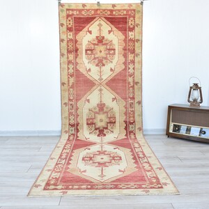 Puede incluir: Una alfombra de pasillo vintage con un esquema de color rojo y crema. La alfombra tiene un patrón geométrico con una forma de diamante central y detalles intrincados.
