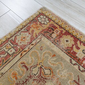 Puede incluir: Una alfombra vintage con fondo beige y borde rojo, naranja y amarillo. La alfombra tiene un patr&oacute;n floral en el centro.