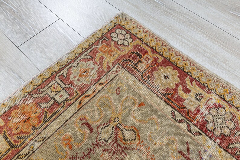 Puede incluir: Una alfombra vintage con fondo beige y borde rojo, naranja y amarillo. La alfombra tiene un patr&oacute;n floral en el centro.