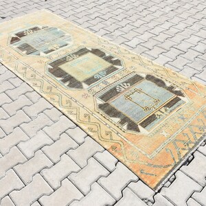 May include: A vintage runner rug with a light beige background and three geometric patterns in shades of blue, brown, and beige.