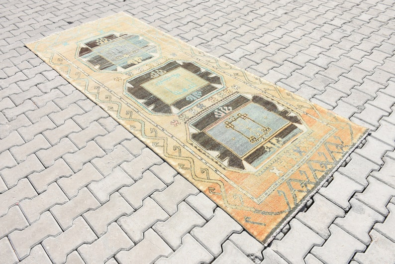 May include: A vintage runner rug with a light beige background and three geometric patterns in shades of blue, brown, and beige.