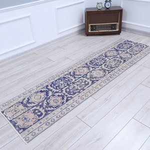 Op de afbeelding: Een vintage loper met een crèmekleurige achtergrond en een blauw en roze bloemenpatroon. De loper heeft een verweerde look en is perfect om een ​​bohemien touch aan je huis toe te voegen.