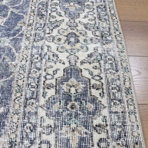 May include: A vintage rug with a cream and blue floral pattern. The rug has a distressed look and is made of a woven material.
