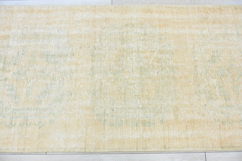 May include: A light beige rug with a faded green pattern in the center. The rug has a distressed look and is made of a soft, woven material.