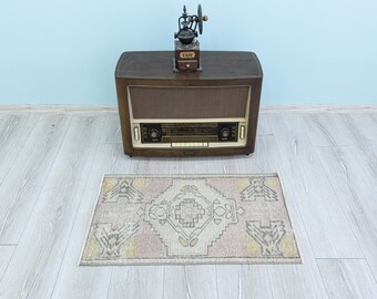 May include: A vintage wooden radio with a speaker grille and a coffee grinder on top. The radio is sitting on a light wood floor with a small rug with a geometric pattern in beige, pink, and yellow.