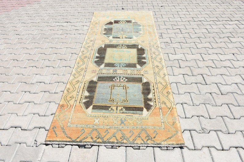 May include: A vintage Turkish runner rug with a geometric pattern in shades of beige, blue, and brown. The rug has a fringe border and is laid out on a gray concrete surface.