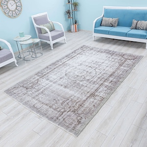 Puede incluir: Una alfombra vintage de color marrón claro con un patrón floral descolorido. La alfombra está colocada sobre un suelo de madera claro en un salón.