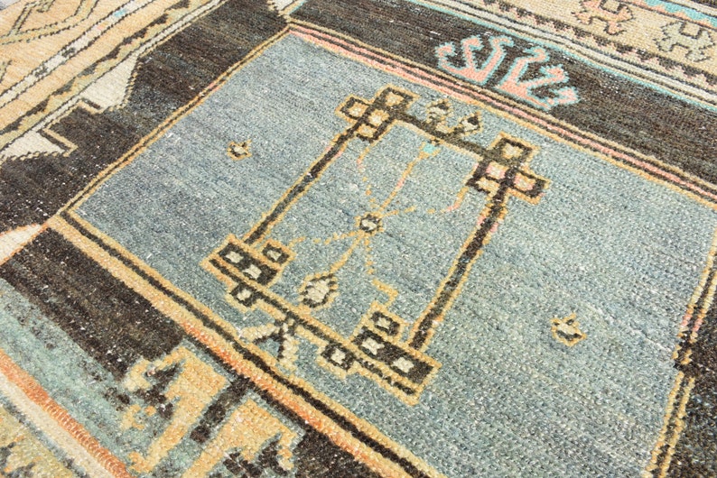 May include: A close-up of a blue and brown rug with a geometric pattern. The rug has a light blue center with a brown border and a geometric design in the center.