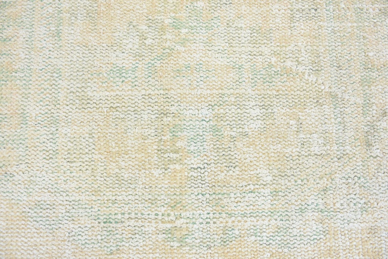 May include: Close-up of a beige woven fabric with a subtle green pattern. The fabric has a textured, slightly rough surface.