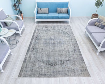 May include: A gray and white vintage rug with a floral pattern. The rug is laid out on a white wood floor in a living room setting with white furniture.