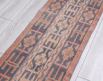 May include: A vintage runner rug with a geometric pattern in shades of pink, orange, and gray. The rug has a distressed look and is perfect for adding a touch of bohemian style to any room.