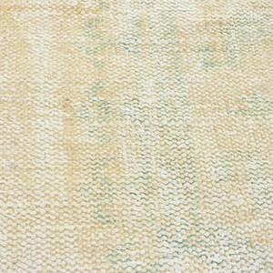 May include: Close-up of a cream-colored woven rug with a subtle green pattern. The rug has a textured surface and a slightly distressed look.
