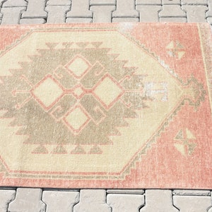 Puede incluir: Una alfombra vintage con un patr&oacute;n geom&eacute;trico en tonos rosa, beige y gris. La alfombra tiene un aspecto desgastado y es perfecta para a&ntilde;adir un toque de estilo bohemio a cualquier habitaci&oacute;n.