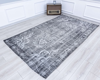 May include: A vintage-style rug with a faded, distressed look. The rug has a black background with a white floral pattern. The rug is laid out on a light wood floor.