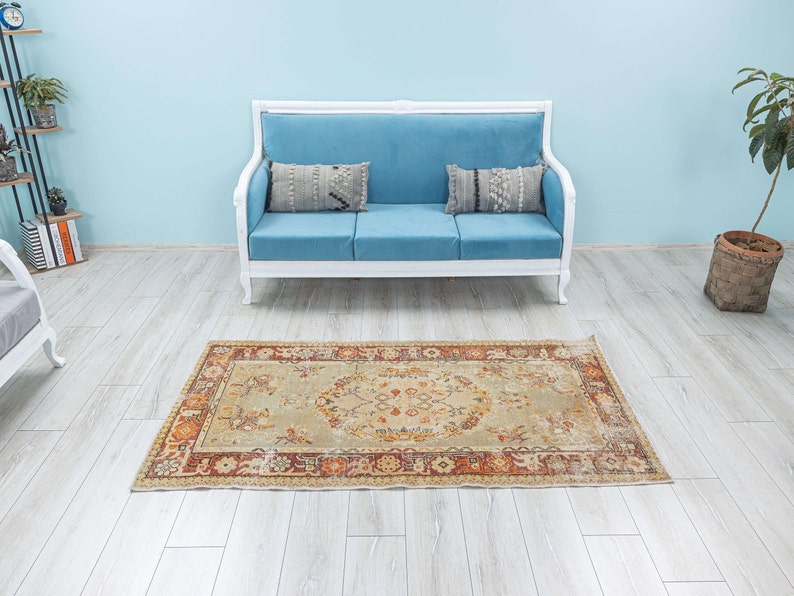 Puede incluir: Un sof&aacute; azul claro con dos almohadas se encuentra sobre una alfombra beige claro con un patr&oacute;n floral. La alfombra tiene un borde rojo, naranja y marr&oacute;n.