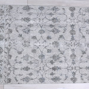 May include: A white rug with a gray floral pattern. The rug has a distressed look and is made of a soft, woven material.