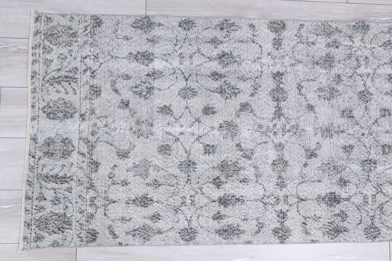 May include: A white rug with a gray floral pattern. The rug has a distressed look and is made of a soft, woven material.