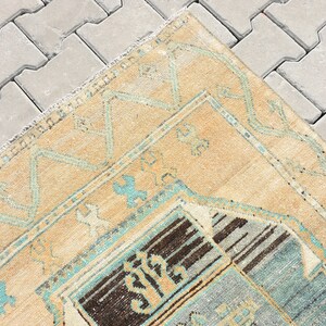 May include: A vintage rug with a beige background and a blue and brown geometric pattern. The rug has a frayed edge and is lying on a gray concrete surface.
