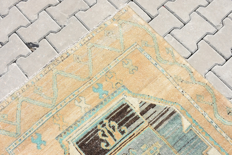 May include: A vintage rug with a beige background and a blue and brown geometric pattern. The rug has a frayed edge and is lying on a gray concrete surface.