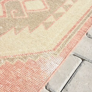 Puede incluir: Una alfombra de color rosa y beige con un dise&ntilde;o geom&eacute;trico. La alfombra est&aacute; sobre una superficie de hormig&oacute;n gris.