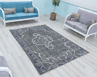 May include: A vintage style rug with a faded blue and gray color scheme. The rug has a floral pattern in the center and a border with a geometric design. The rug is laid out on a light wood floor.