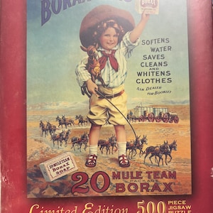 Può includere: Una scatola di puzzle in stile vintage con una pubblicità retrò per Borax. L'immagine presenta un bambino con un cappello da cowboy che tiene in mano una scatola di Borax, con la scritta "Borax is King". Il puzzle è un'edizione limitata di 500 pezzi.