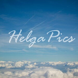 Puede incluir: Una vista aérea de un cielo azul brillante con nubes blancas y esponjosas. El texto "Helga Pics" está escrito en cursiva en el cielo. Una capa de nubes blancas en la parte inferior.