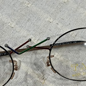 May include: Black round eyeglasses with gold accents and a multi-colored temple. The glasses have a clear lens and say "MADE IN ITALY CE" on the side.