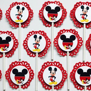 Puede incluir: Doce adornos para cupcakes rojos y blancos con una imagen de dibujos animados de Mickey Mouse. Cada adorno tiene un borde rojo festoneado.