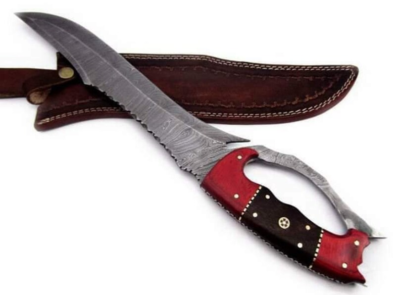 May include: A Damascus steel knife with a red and black wood handle. The knife has a curved blade and a leather sheath.