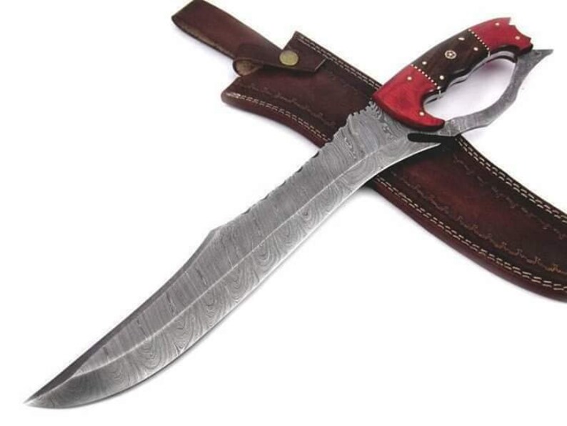 May include: A large, curved, Damascus steel knife with a red and brown wood handle. The knife has a leather sheath with stitching.