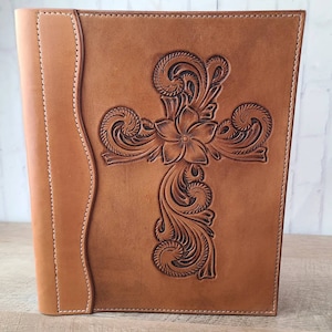 May include: A brown leather journal with a tooled design of a cross with floral accents.