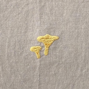 May include: Two embroidered yellow mushrooms on a gray fabric background.