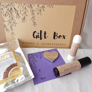 May include: A gift box labelled "Gift Box Number 9 Aromatherapy" contains a bag of chamomile tea, a lip balm, a roller bottle of "Sleep Blend" aromatherapy, and a purple card with a heart-shaped note that says "love you".