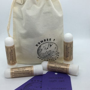May include: A set of four essential oil inhalers in a white drawstring bag. The inhalers are labelled "Stress", "Sleep", "Uplift", and "Motivate". The set also includes a purple tag that says "Inhaler Gift Set" and "4 Inhalers Stress, Sleep, Uplift & Motivate".