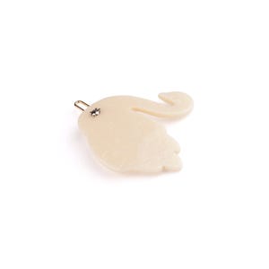 Puede incluir: Pinza para el pelo de color marfil con forma de elefante. La pinza tiene un pasador de metal dorado y un pequeño adorno plateado. El diseño del elefante es liso y tiene una trompa curvada y una cabeza detallada.