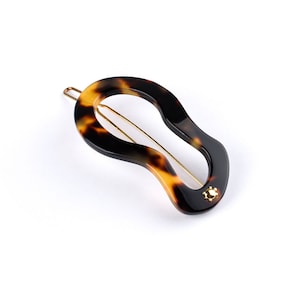 May include: A tortoiseshell hair clip with a gold accent. The clip is shaped like a teardrop and has a smooth, glossy finish.