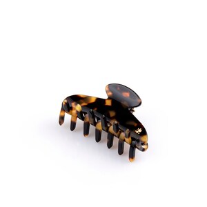 Peut inclure: Une pince à cheveux en écaille de tortue avec un accent doré. La pince a une forme unique et est conçue pour maintenir les cheveux en place de manière sécurisée.