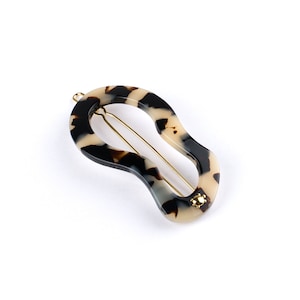 May include: A tortoiseshell hair clip with a gold metal bar and a gold metal accent. The clip is shaped like a teardrop.