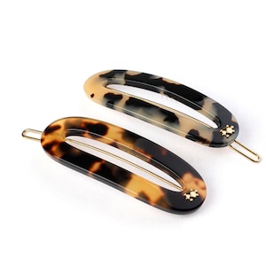 Peut inclure: Deux pinces à cheveux en écaille de tortue avec des accents dorés. Les pinces sont de forme ovale avec une finition lisse et brillante.