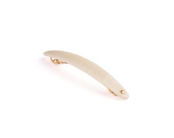 May include: A curved hair barrette featuring a smooth, off-white, matte-textured top surface. The accessory includes a gold-toned metal clasp mechanism visible underneath, with a small gold-toned rivet detail at one end of the barrette.
