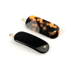 May include: Two hair clips, one black and one brown with a tortoiseshell pattern. Both clips have a gold accent.