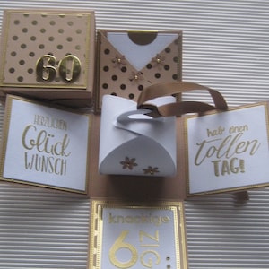 Könnte beinhalten: Eine weiße Box mit einem goldenen Band und goldenen Akzenten. Die Box hat sechs Seiten, jede mit einem anderen Design. Eine Seite hat eine goldene Zahl 60, eine andere Seite hat den Text "Herzlichen Glückwunsch", eine andere Seite hat den Text "Hab einen tollen TAG!" und eine andere Seite hat den Text "knackige 60".