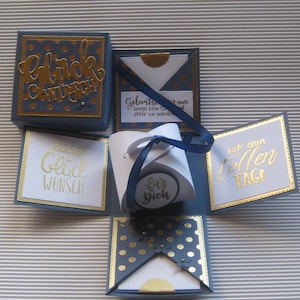 Könnte beinhalten: Eine blaue und goldene Explosionsbox mit den Worten "Glückwunsch", "Herzlichen Glückwunsch", "für dich" und "Hab einen tollen Tag!" Die Box ist mit goldenen Punkten und einem blauen Band verziert.