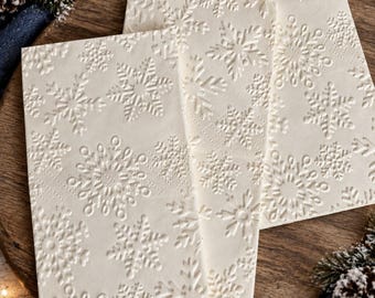 Könnte beinhalten: Drei rechteckige, cremeweiße Papierkarten mit einem geprägten Muster aus verschiedenen Schneeflockendesigns. Die Karten sind leicht überlappend angeordnet und zeigen die erhabene Textur der winterlichen Motive auf der Oberfläche jedes Stücks.