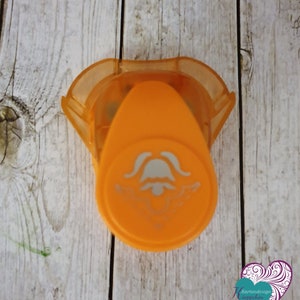 Könnte beinhalten: Orangefarbener Plastik-Bastelstanzer mit einem Glockendesign. Der Stanzer wird verwendet, um dekorative Formen in Papier zu erstellen.