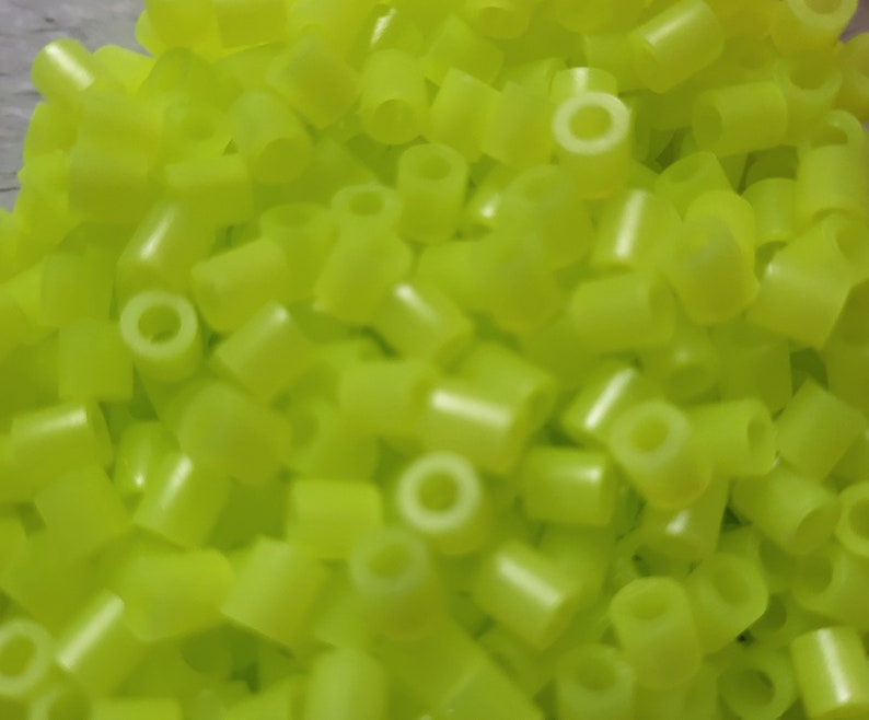 May include: A large pile of bright yellow plastic beads. The beads are small and cylindrical with a hole in the center.