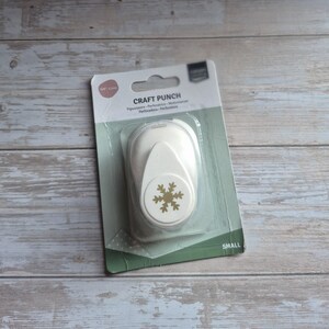 Könnte beinhalten: Ein weißer Bastelstanzer mit einem goldenen Schneeflocken-Design, verpackt in einer transparenten Blisterverpackung. Die Verpackung enthält den Text "CRAFT PUNCH" und "SMALL". Der Stanzer ist für Papierbasteln und Scrapbooking gedacht.